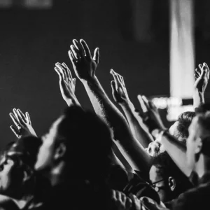 Dynamic black and white photo of a concert audience with hands raised, capturing the energy of live music.